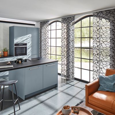 Küchenzeile in schwarz-Grau mit Fassadenfenstern und weiß-schwarz gemusterten Flächenvorhängen.
