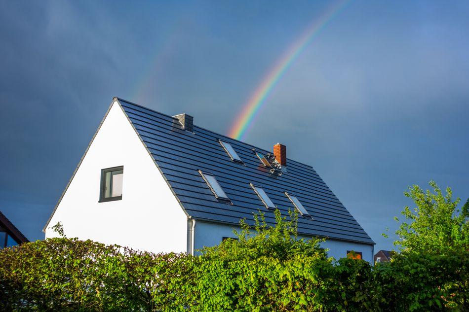Weißes Haus vor gewittrigem Himmel mit Regenbogen