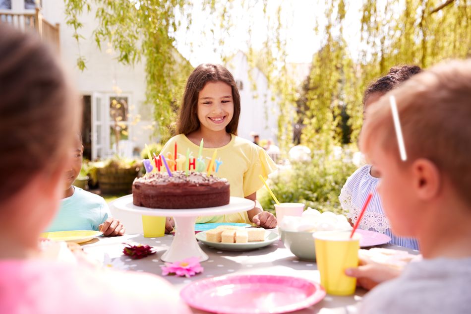 Kindergeburtstagstisch umringt von kleinen Gästen mit Kuchen und Kerzen in der Mitte.