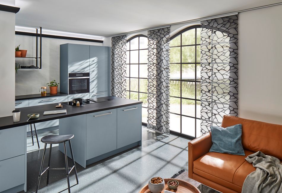 Küchenzeile in schwarz-Grau mit Fassadenfenstern und weiß-schwarz gemusterten Flächenvorhängen.