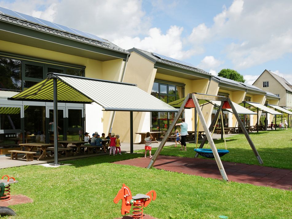 Referenzbild von fünf markilux syncra mit gestreiften Tüchern. Darunter spielen Kinder.