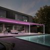 Pergolamarkise markilux style an einem modernen, schicken Kubusgebäude. Die pinke Beleuchtung der Pergola taucht die Terrasse und den Garten mit Pool in schönes Licht.